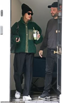 a man and woman walking out of a door with drinks in their hands while wearing beanies