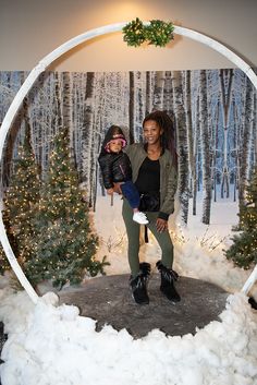 a woman holding a small child in front of a christmas display with snow on the ground