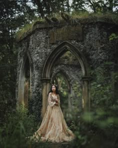 a woman in a long dress is standing near an old stone structure with ivy growing on it