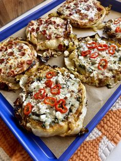 several pizzas with cheese and peppers on a blue tray next to an orange towel