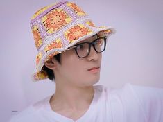 a young man wearing glasses and a crocheted hat with flowers on the brim