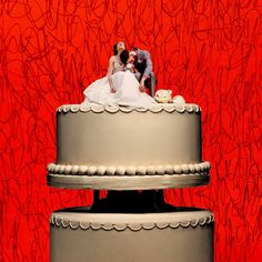 a bride and groom kissing on top of a wedding cake in front of a red wall