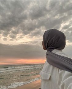 a woman standing on top of a beach next to the ocean under a cloudy sky