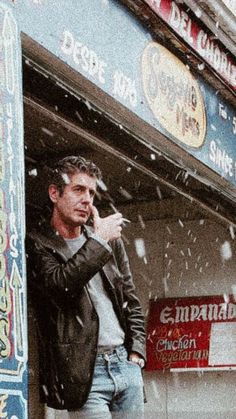 a man standing in front of a store talking on a cell phone while it snows