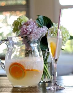 two glasses filled with liquid sitting on top of a table next to flowers and vases