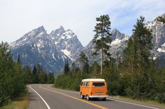 an orange van is driving down the road in front of some snow capped mountain peaks