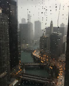 rain is falling down on the window and buildings in the city are seen through it