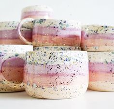 four coffee mugs with different colors and speckles are stacked on top of each other