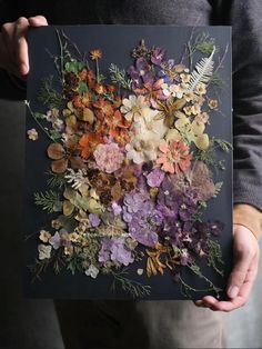 a person holding up a piece of art made out of dried flowers and foliages