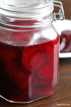 a jar filled with pickled red onions on top of a wooden table next to a plate