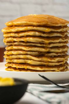 a stack of pancakes sitting on top of a white plate next to a bowl of butter