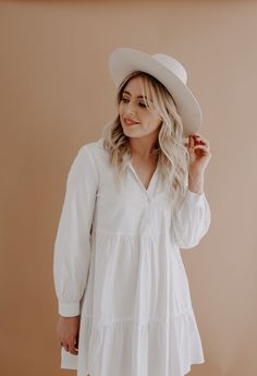 a woman wearing a white dress and hat with her hands in her pockets, looking off to the side