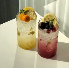 two glasses filled with drinks sitting on top of a white table next to each other