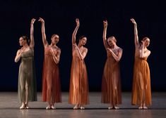 five women in long dresses standing on stage with their arms up and one holding her head