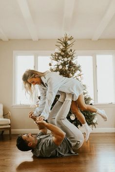 a man and woman are playing with each other in front of a christmas tree on the floor