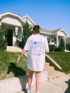 a woman is walking down the sidewalk in front of her house wearing a t - shirt that says i love being 24