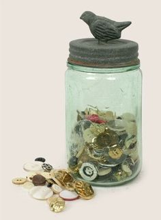 a glass jar filled with lots of different types of coins and a bird sitting on top of it