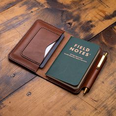 a brown leather notebook with a green field notes book and pen sitting on top of it