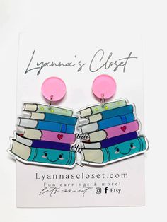 a pair of pink and blue book earrings sitting on top of a white card