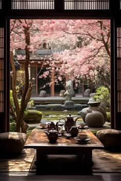 a table with two tea cups on it in front of a tree filled with pink flowers