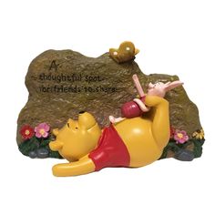 a winnie the pooh figurine laying next to a rock with a quote on it