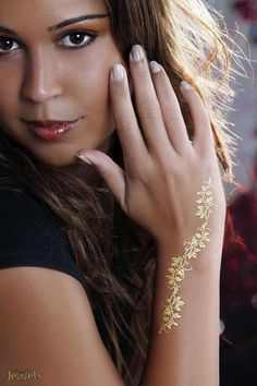 a beautiful woman with gold tattoos on her arm and hand, posing for the camera