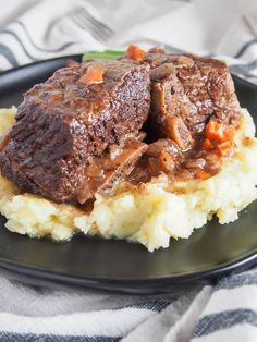 a black plate topped with mashed potatoes and beef on top of gravy