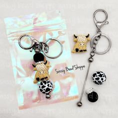 two keychains with cow charms on them sitting next to each other in front of a bag