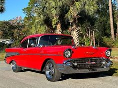 an old red car is parked on the side of the road in front of palm trees