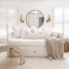 a white daybed with pillows and blankets on it in front of a round mirror