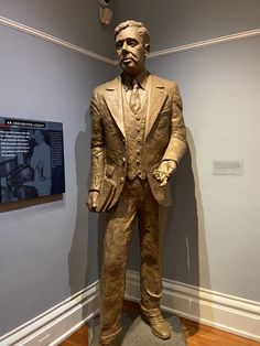 a statue of a man in a suit stands next to a plaque on the wall