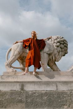 a woman standing next to a statue of a lion on top of a stone structure