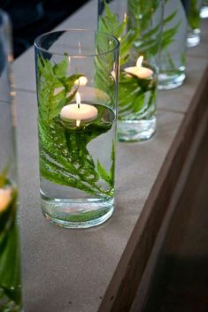 candles are lit in glass vases filled with water and green leafy plants on the table