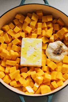 a pot filled with butter and cubed cheese next to a garlic clove on the side