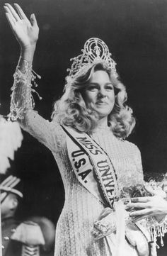 an old black and white photo of a woman wearing a tiara with her hands in the air