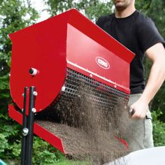 a man is using a red machine to spread dirt on top of a truck bed