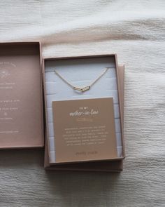 an open box with a necklace in it on top of a white bedcloth covered surface