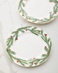 two plates decorated with pine branches and red berries on white marble counter top, one has gold trim