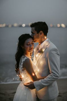 a man and woman standing next to each other in front of the ocean at night