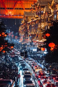 many cars are parked on the street in front of tall buildings and lanterns hanging from the ceiling