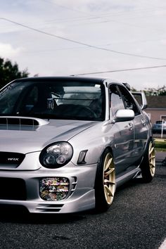 a silver car parked on the side of a road next to another car with gold rims