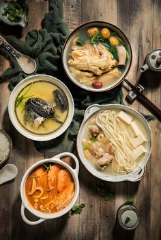 several bowls of food are arranged on a wooden table with chopsticks and utensils