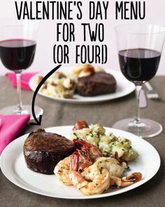 two white plates topped with meat and shrimp next to wine glasses filled with red wine