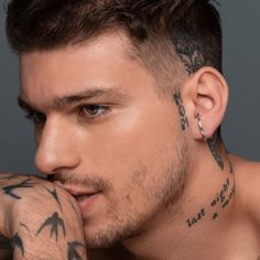 a man with tattoos and piercings on his face is posing for the camera while holding his hand to his chin