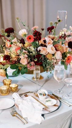 the table is set with white and gold plates, silverware, and floral centerpieces