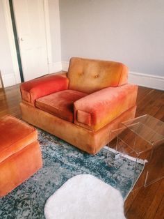 an orange couch and chair in a room with hardwood floors, rugs and glass tables