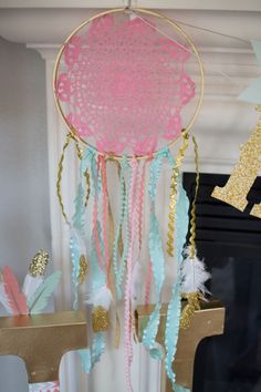 a pink, blue and gold dream catcher hanging from the ceiling in front of a fireplace