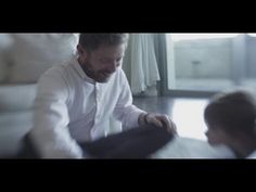 a man sitting on the floor next to a little boy in white shirt and black pants