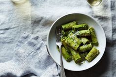 a white bowl filled with green vegetables next to a glass of wine and silverware