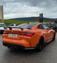 an orange bmw sports car parked in a parking lot with other cars behind it on a cloudy day